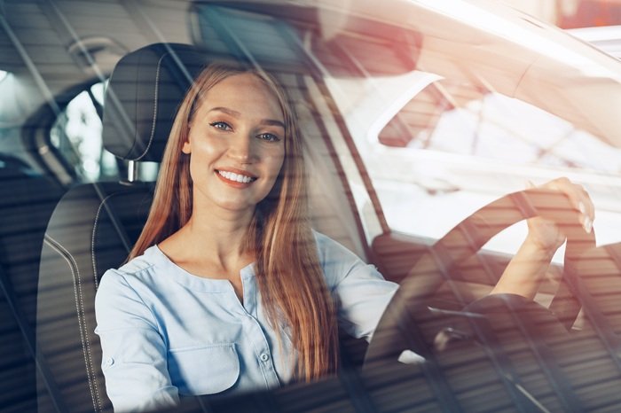 Attractive young woman sitting in new car in showroom close up